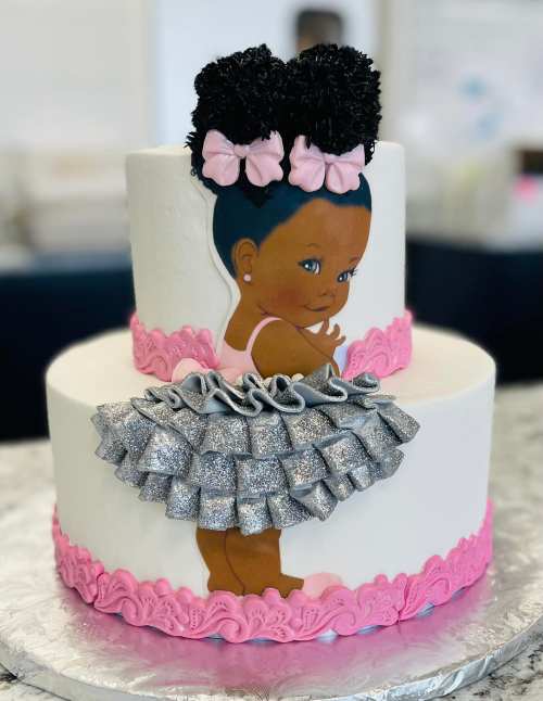 A two-tiered cake featuring a girl with puffy hair, wearing a pink and silver tutu, decorated with bows and pink icing.