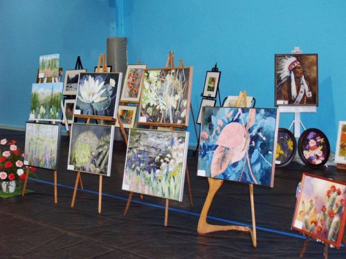 A display of various paintings on easels in a blue room, featuring floral and nature themes.