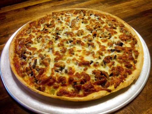 A freshly baked pizza with a golden crust, topped with melted cheese, sausage, and mushrooms on a silver pizza tray.