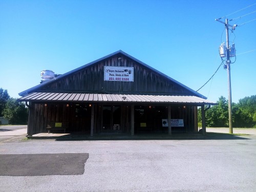 A rustic wooden building with a metal roof, featuring a sign for a restaurant and a clear blue sky above.