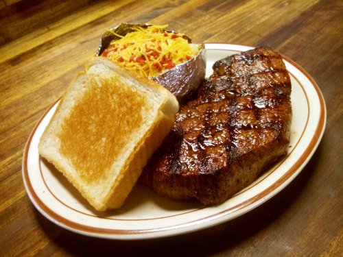 A plate featuring a grilled steak, a baked potato topped with cheese, and two slices of toasted bread.