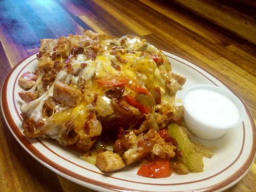 A plate of loaded nachos topped with cheese, grilled chicken, peppers, and a side of ranch dressing.