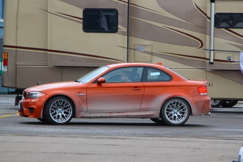 An orange BMW coupe parked on a street, slightly dirty, with an RV in the background.