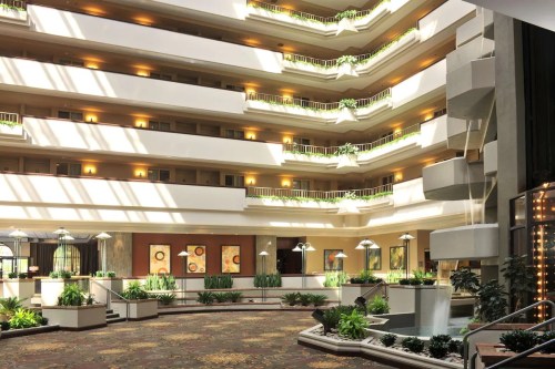 Bright atrium of a hotel with multiple floors, greenery, and natural light streaming through large windows.