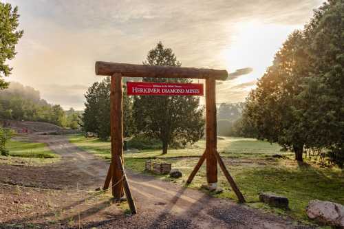 A wooden sign welcomes visitors to Herkimer Diamond Mines, surrounded by trees and a sunrise in the background.