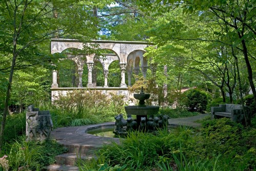 A serene garden scene featuring a stone fountain, lush greenery, and a decorative archway in the background.