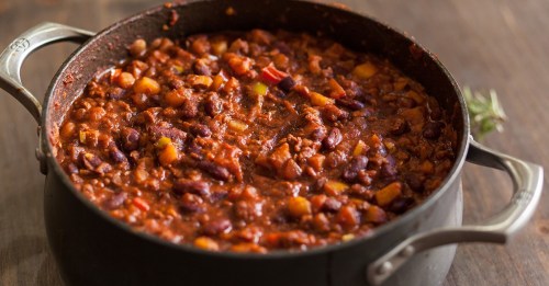 A pot of hearty chili with beans and vegetables, simmering on a wooden surface.
