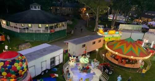 Aerial view of a carnival with colorful rides, food stalls, and a gazebo surrounded by trees at night.