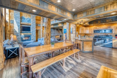 Cozy wooden dining area with a large table, open kitchen, and living space featuring a stone fireplace.
