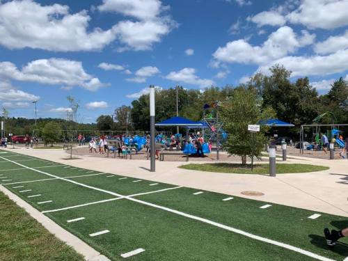 A playground with blue equipment, children playing, and a grassy area under a partly cloudy sky.