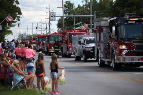 A parade featuring fire trucks and emergency vehicles, with spectators watching along the roadside.