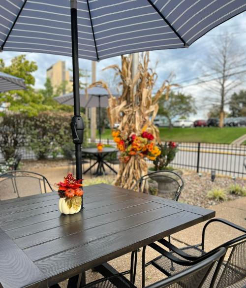 A patio table with a flower arrangement under a striped umbrella, surrounded by autumn decorations and greenery.