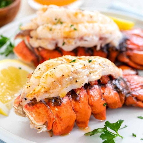 Close-up of cooked lobster tails on a plate, garnished with lemon slices and parsley.