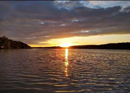 A serene sunset over a calm lake, with golden light reflecting on the water and clouds in the sky.