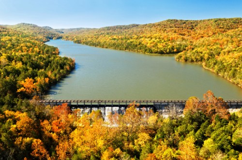 A scenic view of a river winding through autumn-colored hills and trees under a clear blue sky.