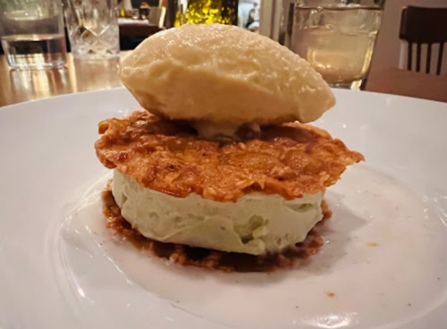 A dessert featuring a crispy topping, creamy green filling, and a scoop of vanilla ice cream on a white plate.