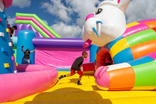 A child runs past a colorful inflatable bunny at a bounce house event, with adults supervising in the background.