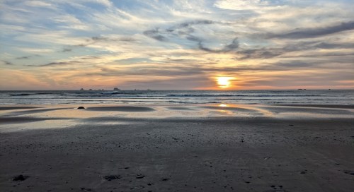 A serene beach at sunset, with gentle waves and a colorful sky reflecting on the wet sand.
