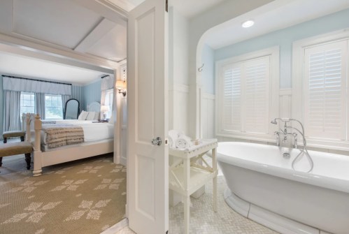 A bright, airy bathroom with a freestanding tub, leading to a cozy bedroom with a bed and soft decor.