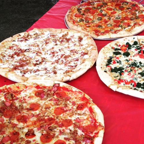 Four pizzas on a red tablecloth: pepperoni, white sauce, veggie, and a meat-lovers variety.