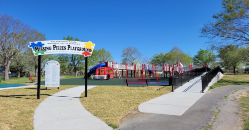 Colorful playground with slides and climbing structures, surrounded by green grass and trees, under a clear blue sky.