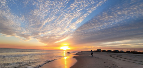 A serene beach at sunset, with vibrant clouds and a person walking along the shore.