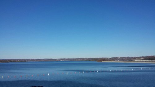 A serene lake under a clear blue sky, with gentle ripples and distant hills on the horizon.