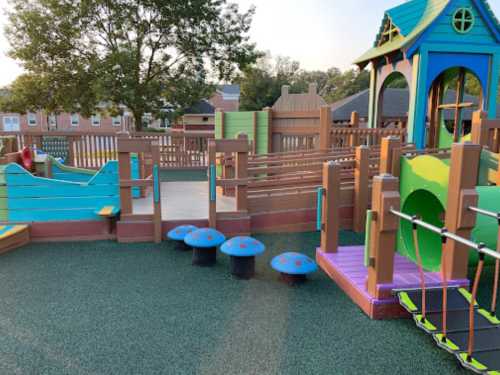 Colorful playground with slides, climbing structures, and mushroom-shaped seating on a rubber surface.