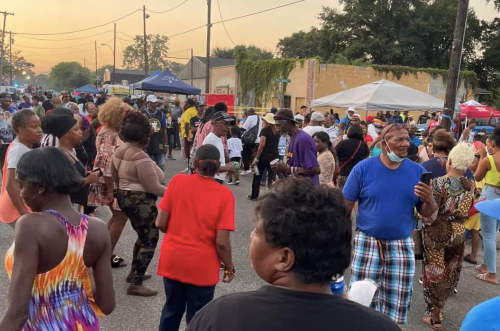A lively street scene with a large crowd dancing and socializing during an outdoor event at sunset.