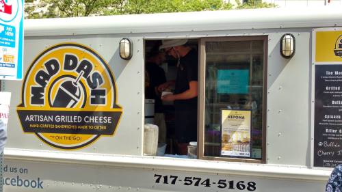 A food truck named "Mad Dash" serving artisan grilled cheese sandwiches, with staff preparing orders inside.
