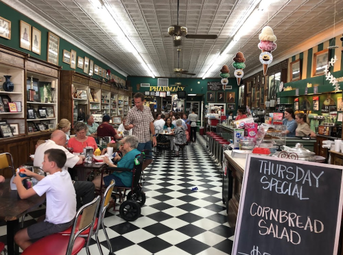 A bustling diner with patrons enjoying meals, vintage decor, and a chalkboard special for cornbread salad.