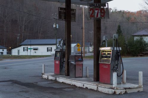 Abandoned gas station with two pumps, a price sign reading 2.79, and a quiet rural background at dusk.