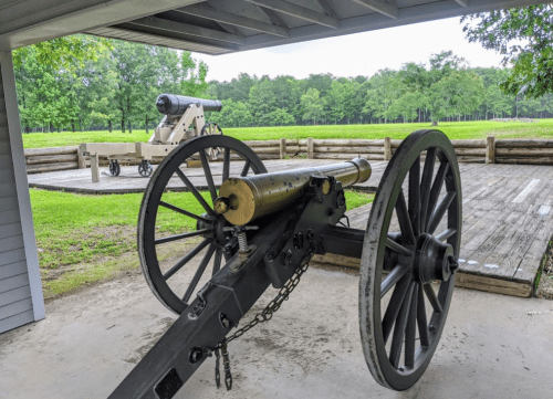 Two historical cannons are displayed outdoors, surrounded by green trees and a wooden platform.
