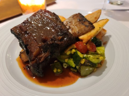 A plate featuring tender beef brisket, crispy potatoes, and a colorful vegetable medley in a rich sauce.