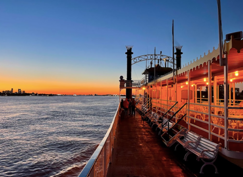 A riverboat docked at sunset, with warm lights glowing and a calm water surface reflecting the colorful sky.