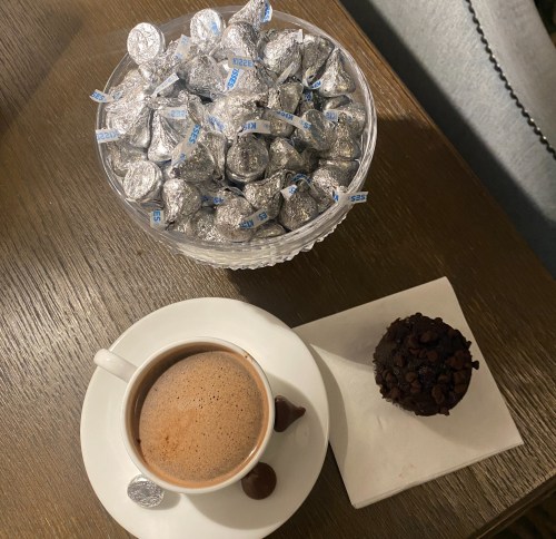 A bowl of silver-wrapped chocolates beside a cup of coffee and a chocolate muffin on a small plate.