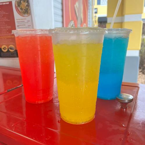 Three colorful drinks in clear cups: red, yellow, and blue, placed on a red table.