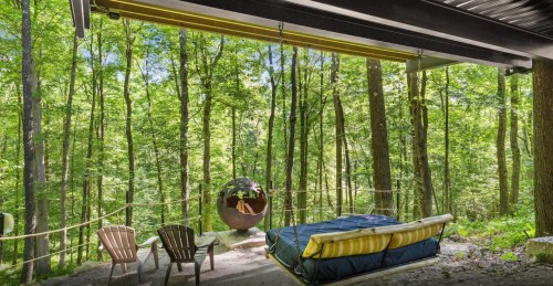 Cozy outdoor seating area with a sofa and chairs, surrounded by lush green trees in a serene forest setting.