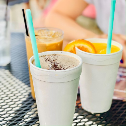 Three drinks on a table: a chocolate shake, iced coffee, and orange juice, all with colorful straws.