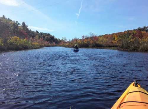 A person kayaking on a calm river surrounded by colorful autumn foliage and clear blue skies.