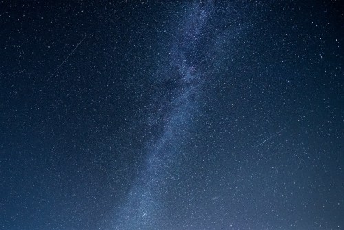 A starry night sky featuring the Milky Way and several shooting stars.