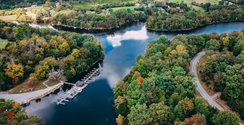 Aerial view of a serene river surrounded by lush greenery and a small marina, with a winding road nearby.