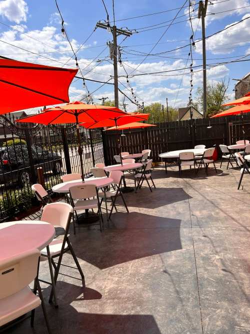 Outdoor dining area with orange umbrellas, empty tables, and a clear blue sky in the background.