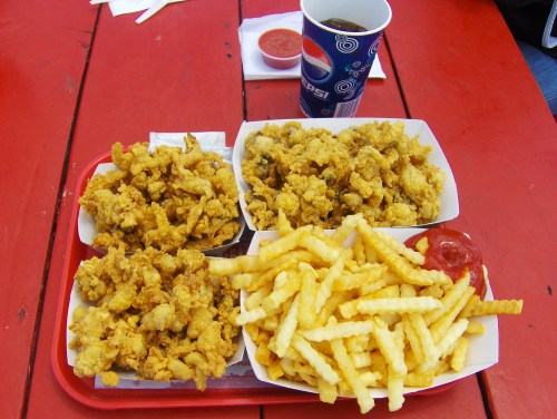 A red tray with two servings of fried food and a side of crinkle-cut fries with ketchup, alongside a drink.