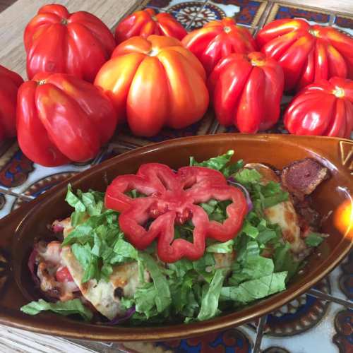 A dish topped with lettuce and a sliced red pepper, surrounded by fresh red tomatoes on a decorative plate.