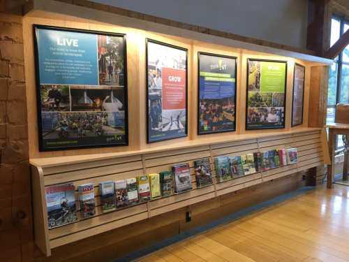 A wooden display featuring informational posters and a rack of brochures in a well-lit indoor space.