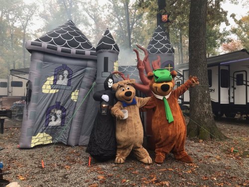 Two costumed characters, Scooby-Doo and Shaggy, pose with a cloaked figure in front of a spooky inflatable castle.