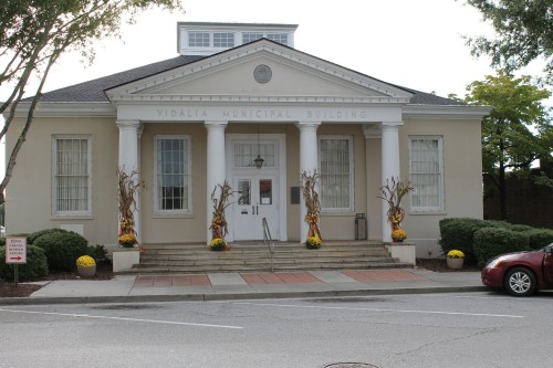 Front view of the Vidalia Municipal Building, featuring columns, decorative corn stalks, and a red car parked nearby.