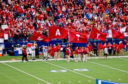 A crowd in red clothing waves large flags on a football field, cheering for their team during a game.