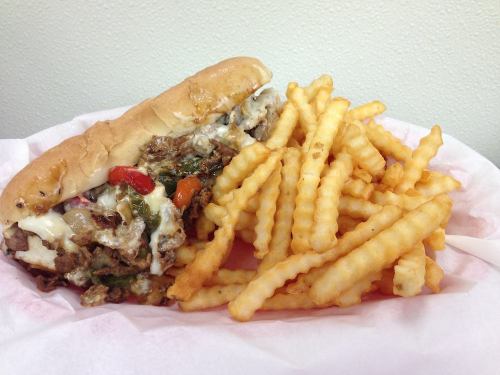 A loaded sandwich with beef, peppers, and cheese, served with a side of crinkle-cut fries in a basket.